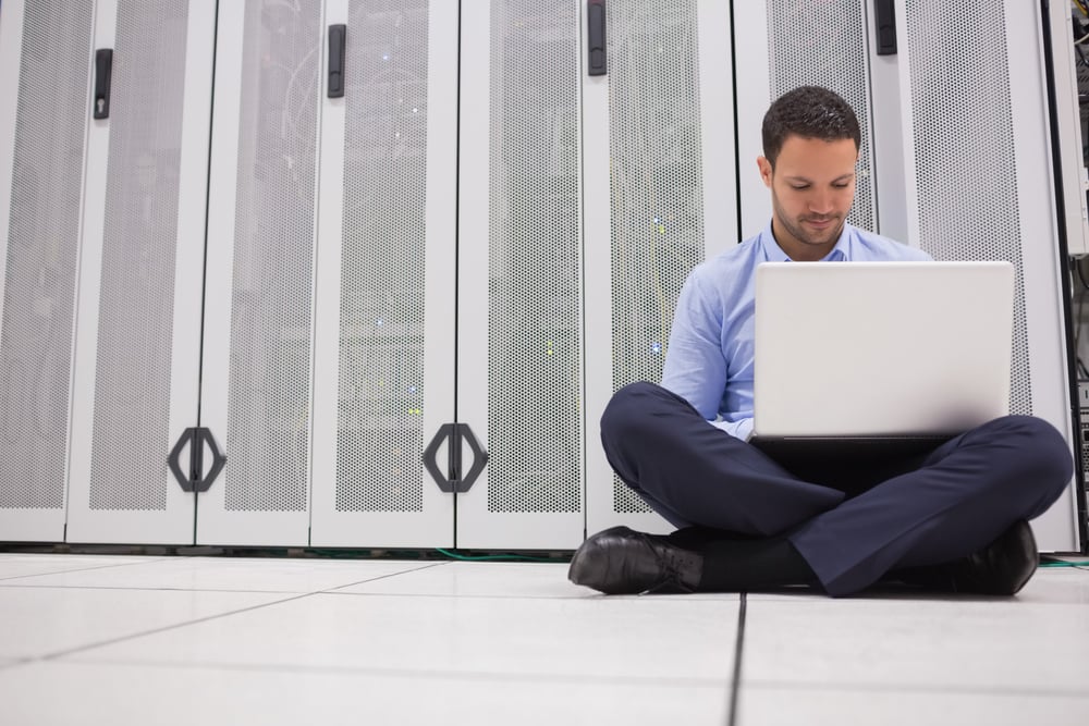 Technician sitting on floor working on laptop in data center