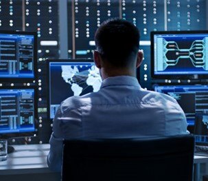 IT technician monitoring global network performance on multiple screens in a control room.