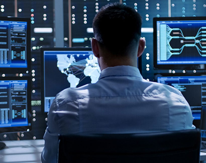 Engineer analyzing 3D network data on multiple monitors in a control room.