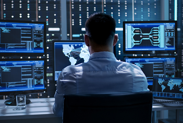 IT technician monitoring network performance on multiple screens in a control room.